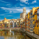Colorful yellow and orange houses and bridge Pont de Sant Agusti reflected in water river Onyar, in Girona, Catalonia, Spain. Church of Sant Feliu and Saint Mary Cathedral at background.
